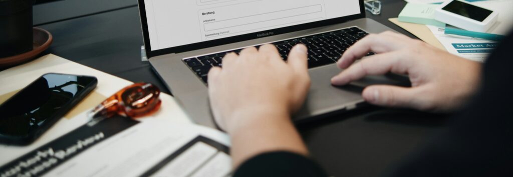 Hände auf einer Laptop-Tastatur mit Geschäftsunterlagen – E-Invoicing in den VAE und Saudi-Arabien