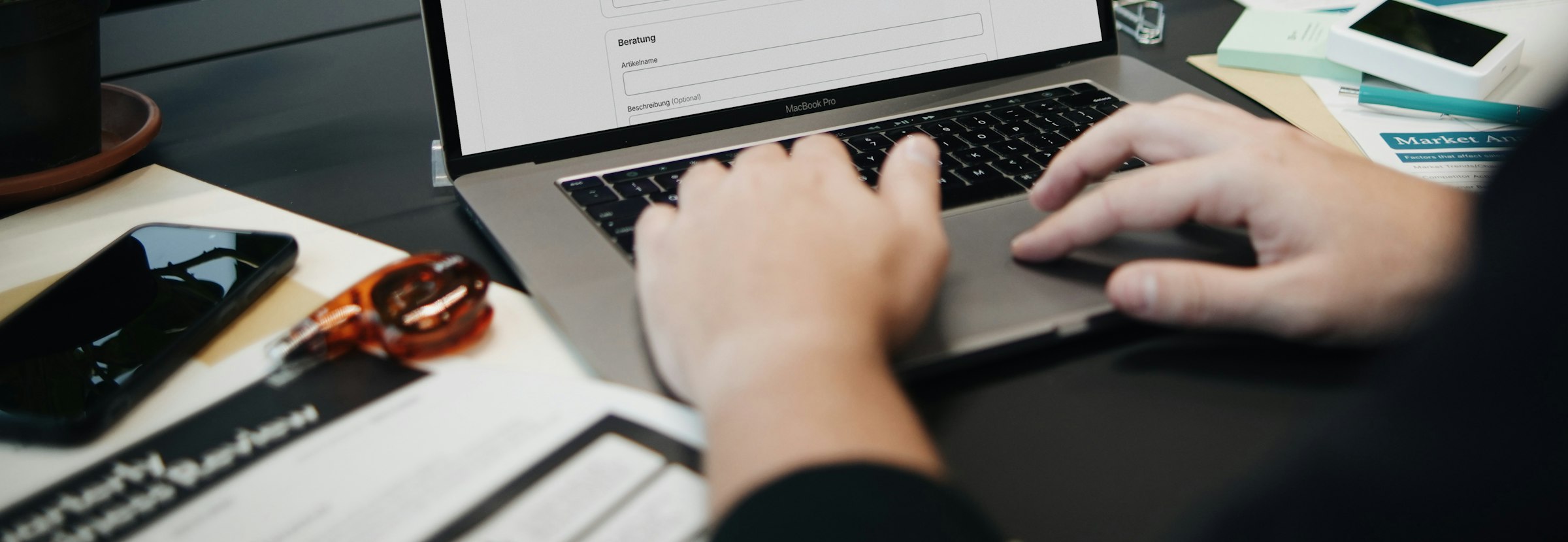 Hände auf einer Laptop-Tastatur mit Geschäftsunterlagen – E-Invoicing in den VAE und Saudi-Arabien